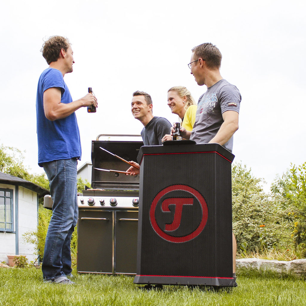 ROCKSTER Fröhliche Freunde am Grill, im Vordergrund ROCKSTER Lautsprecher
