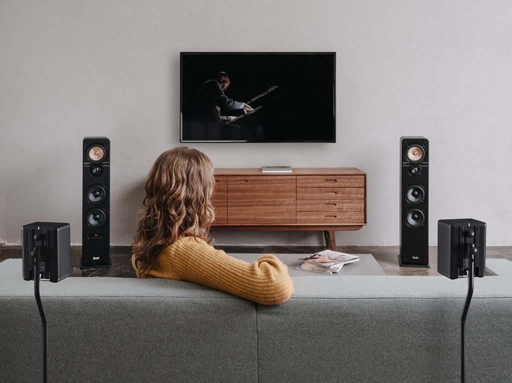 Frau auf Sofa sieht Musiker auf TV-Screen, links und rechts Ultima 40 Standlautsprecher von Teufel