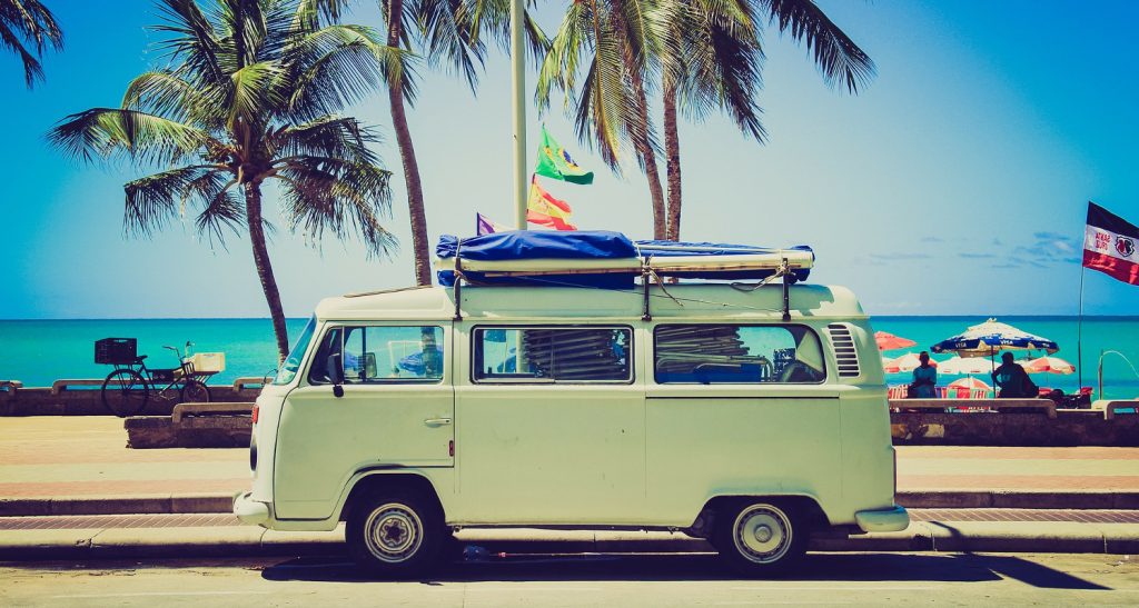 Alter VW-Bulli vor einem Horizont mit Meer und Palmen.