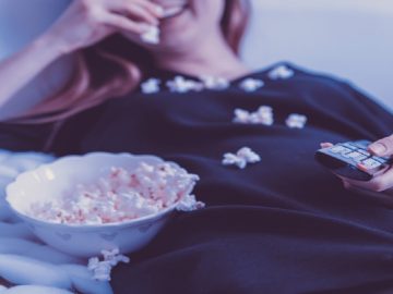 Frau mit Fernbedienung in der Hand sitzt auf Sofa und isst Popcorn