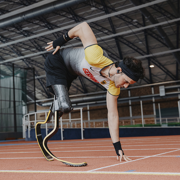 Junger Mann mit Beinprothesen in der Sprint-Startposition in einer Sporthalle.
