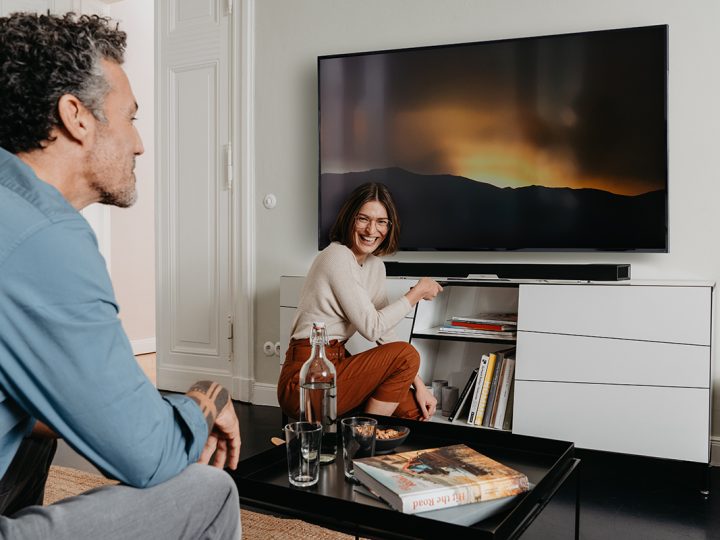 Mann auf Sofa und Frau vor Soundbar und Fernseher