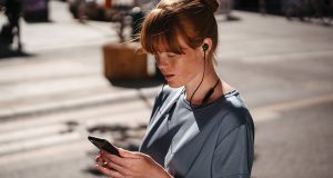 Junge Frau mit Smartphone und In-Ear-Kopfhörern REAL BLUE IN