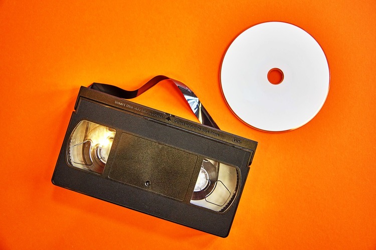 Eine Videokassette und eine CD vor einem orangenen Hintergrund.