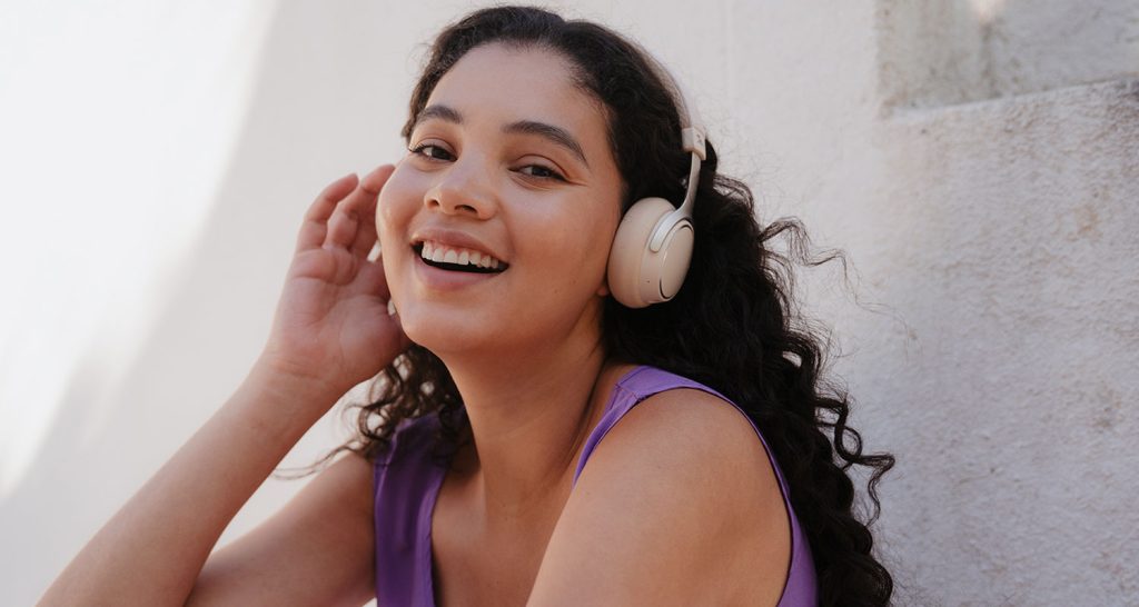A young smiling woman listening to songs with Teufel's SUPREME ON headphones.