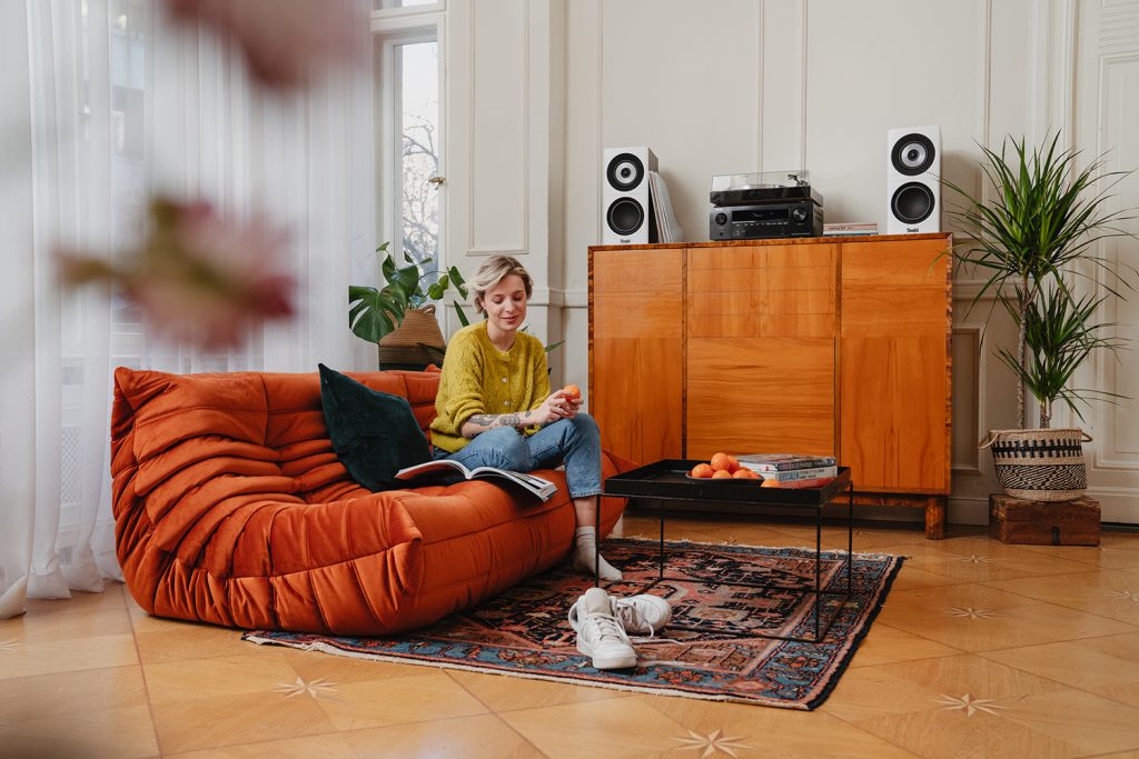 A woman relaxes on the couch at home while listening to records through a Teufel speaker set.