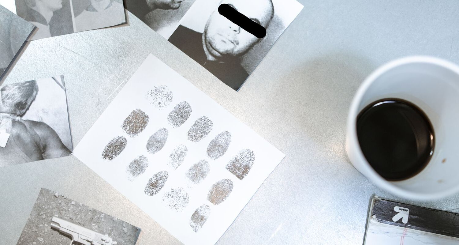 Fingerabdrücke und Schwarz-Weiß-Fotos auf einem Tisch neben einem Becher Kaffee