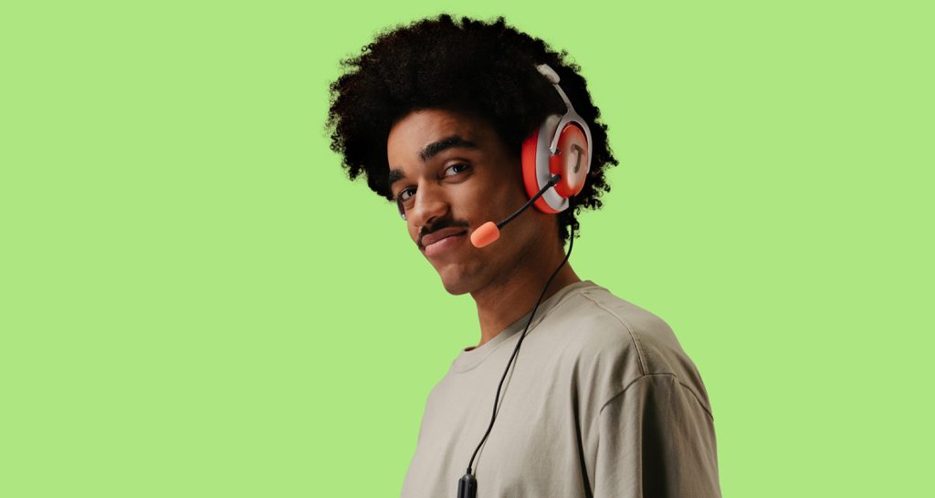 Ein Mann steht vor einem grünen Hintergrund und trägt einen roten Gaming-Kopfhörer.