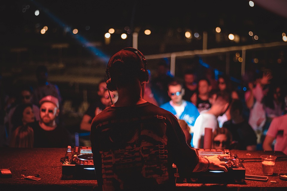 Rückansicht eines DJs, der in einem Club vor Publikum am Controller steht