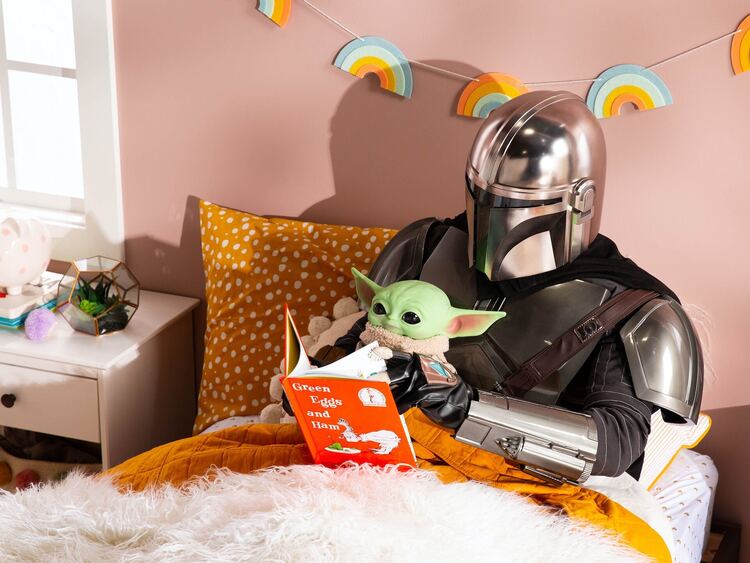 Die beiden Star Wars Charaktere Yoda und The Mandalorian lesen zusammen im Bett ein Buch.