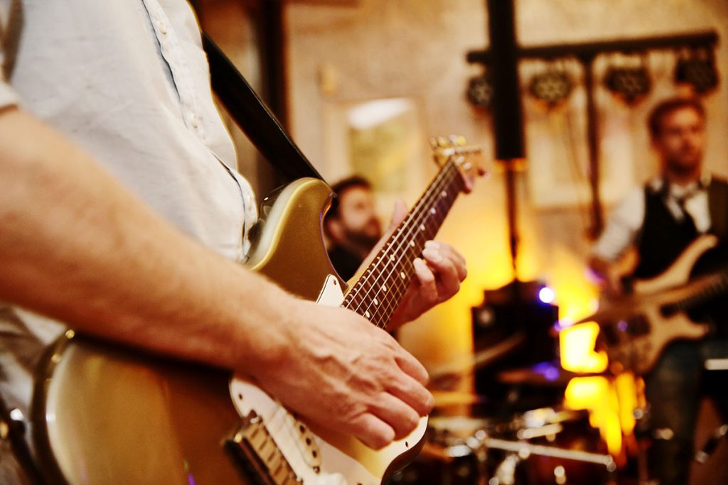 Gitarrist spielt live in einem Raum, im Hintergrund ein Bassist und ein Schlagzeuger