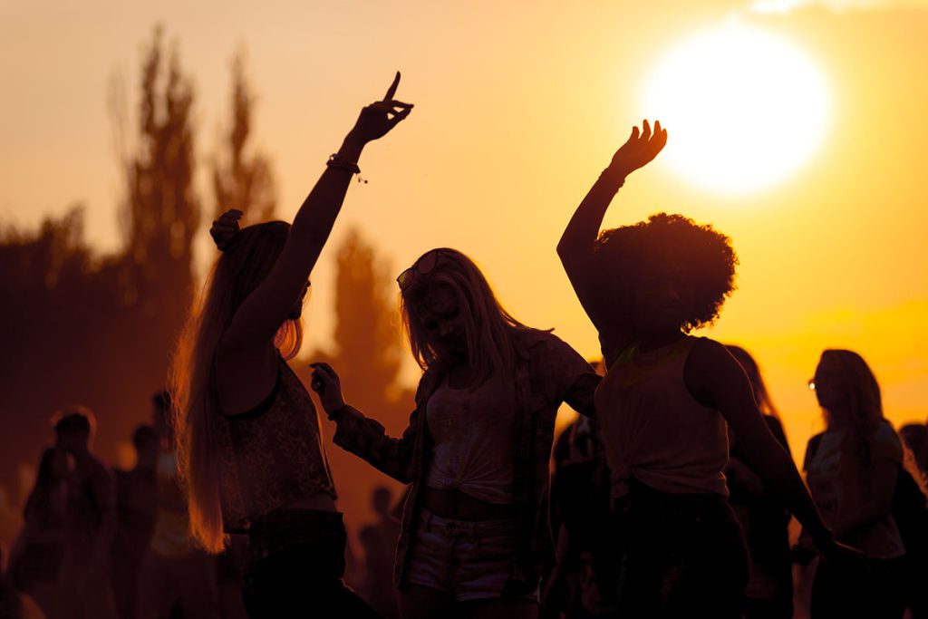 Drei Frauen tanzen auf einem Festival im Sonnenuntergang
