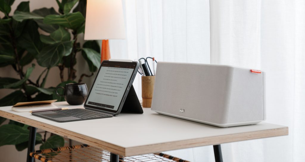 Auf einem Schreibtisch steht ein iPad mit Tastatur und daneben ein moderner Lautsprecher in weiß.