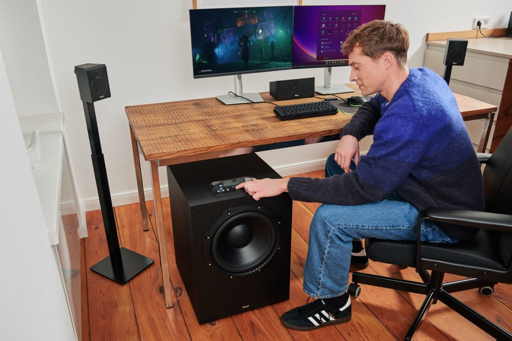 Mann sitz am Tisch mit Gaming-Setup und bedient den CONCEPT 12 Subwoofer von Teufel