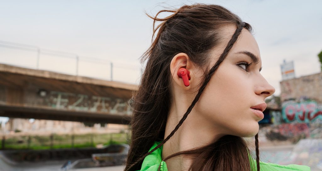 Junge Frau in urbaner Umgebung trägt In-Ears AIRY TWS 2 in Rot