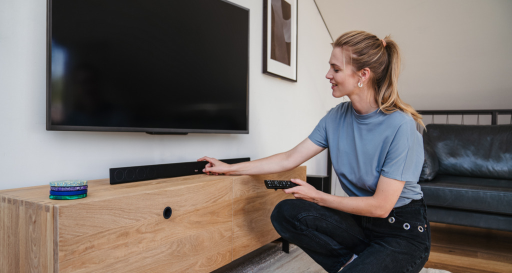 CINEBAR 11 für Dolby Atmos "2.1-Set" Frau im Wohnzimmer mit TV-Fernbedienung und CINEBAR 11 von Teufel