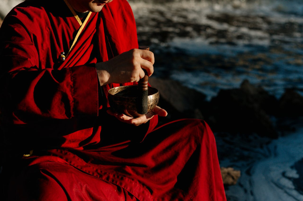 Buddhistischer Mönch in roter Robe spielt eine Klangschale mit einem Holzklöppel