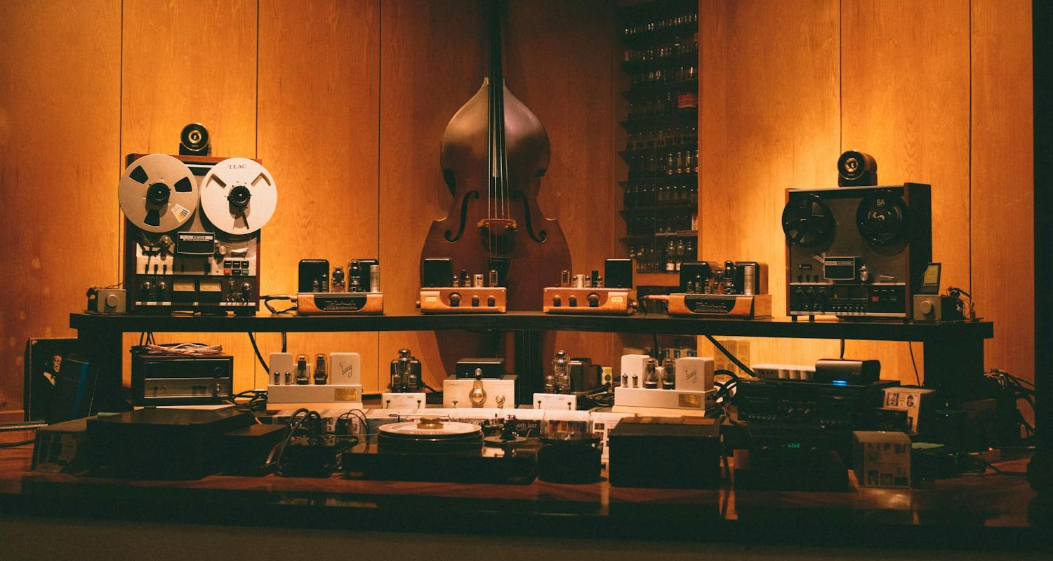 Vintage-HiFi-Setup mit Bandmaschinen, Röhrenverstärkern und Kontrabass in einem warm beleuchteten Hörraum.