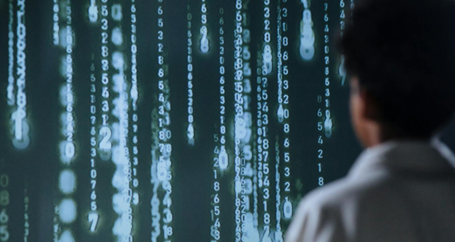 Person betrachtet einen Bildschirm mit herabfallenden Zahlenmustern, die algorithmenbasierte Datenanalyse symbolisieren.