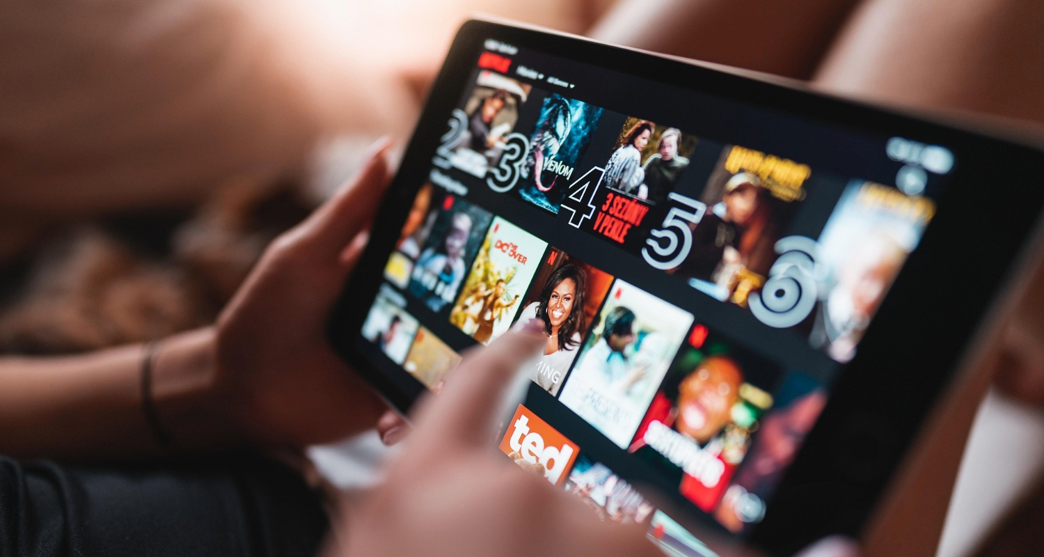 Person hält ein Tablet und scrollt durch die Netflix-Startseite mit verschiedenen Film- und Seriencovern.