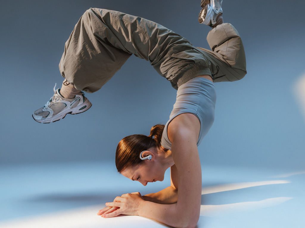 AIRY SPORTS TWS Breakdancer mit Kopfhörern führt vor blauem Hintergrund einen akrobatischen Kopfstand aus.