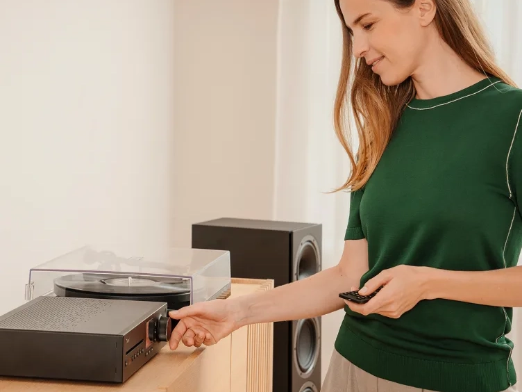 Frau stellt die Lautstärke eines Stereo-Receivers ein, im Hintergrund ein Plattenspieler und Standlautsprecher.