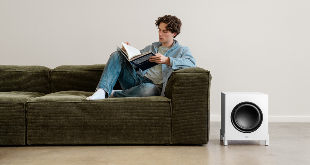 T 10 Mk2 Subwoofer Mann sitzt auf einem Sofa neben einem weißen Teufel T 10 Mk2 Subwoofer